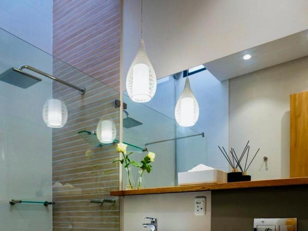 A modern bathroom with a glass shower enclosure, a wooden vanity, and pendant lighting.
