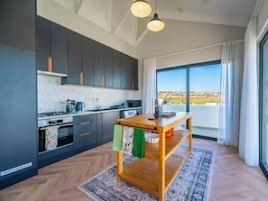 Eine moderne Küche mit dunklen Schränken, einem Holztisch und Blick durch große Fenster.