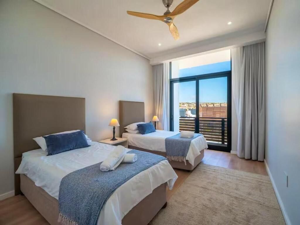 A hotel room with two beds, a ceiling fan, a large window with curtains, and a view of the outside.