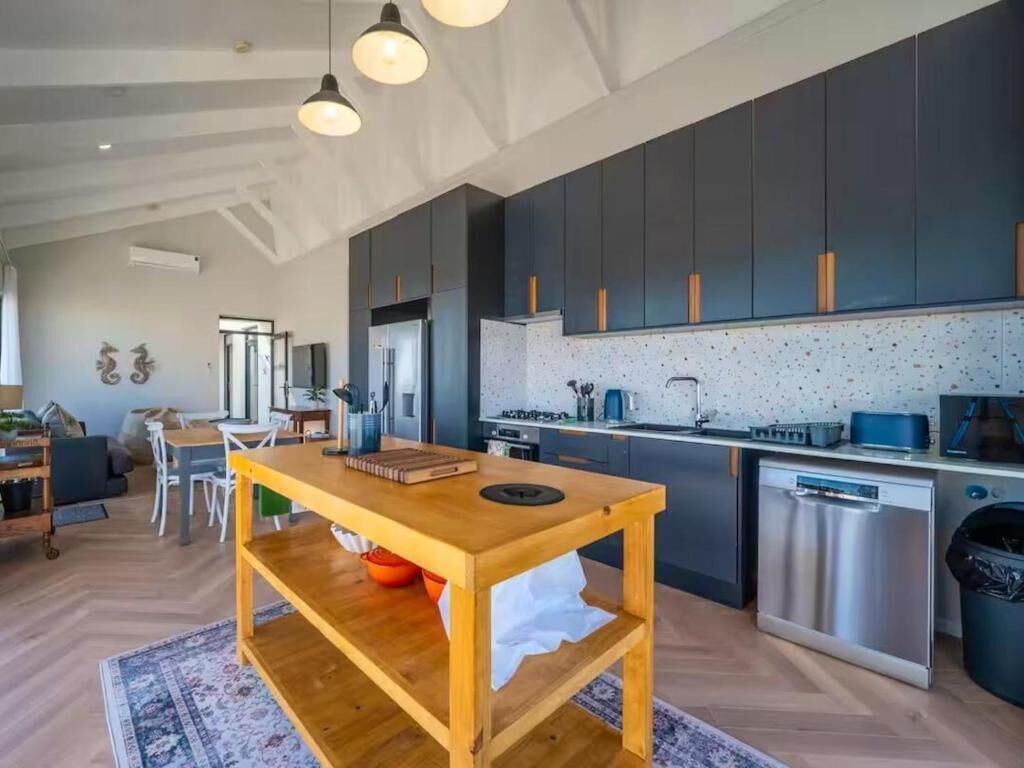 A modern kitchen with dark cabinets, stainless steel appliances, and a wooden table with a rug.