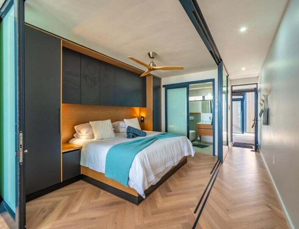 Un dormitorio moderno con cama, cabecero de madera, ventilador de techo y vistas al baño.