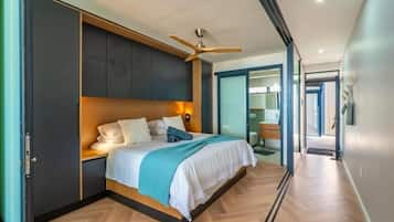 Un dormitorio moderno con cama, cabecero de madera, ventilador de techo y vistas al baño.