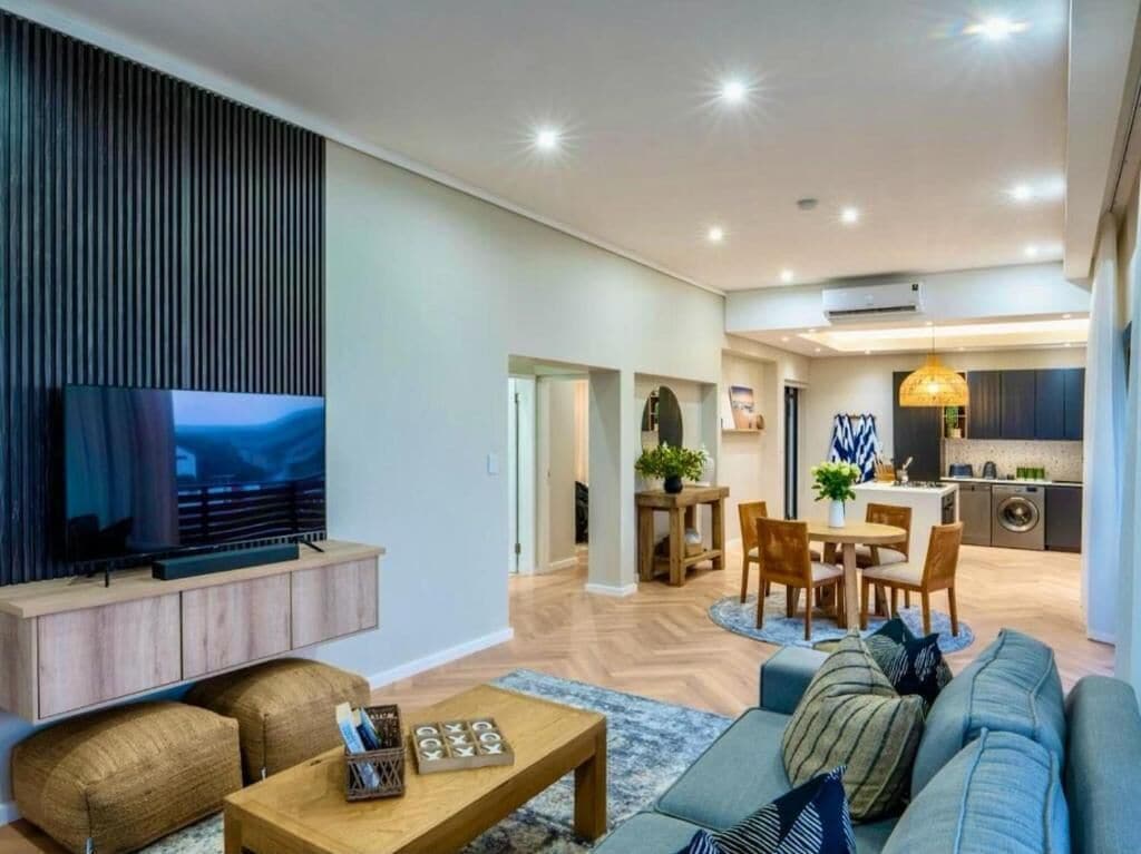 Una sala moderna con una televisión de pantalla plana, un sofá, una mesa de centro y un comedor con mesa y sillas.