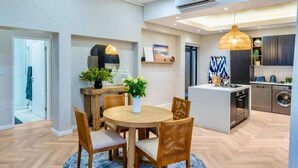 A modern kitchen with a central island, built-in appliances, and a dining area with a round table and chairs. - Kabeljauws Beachfront Luxury Apartments (Jeffreys Bay)