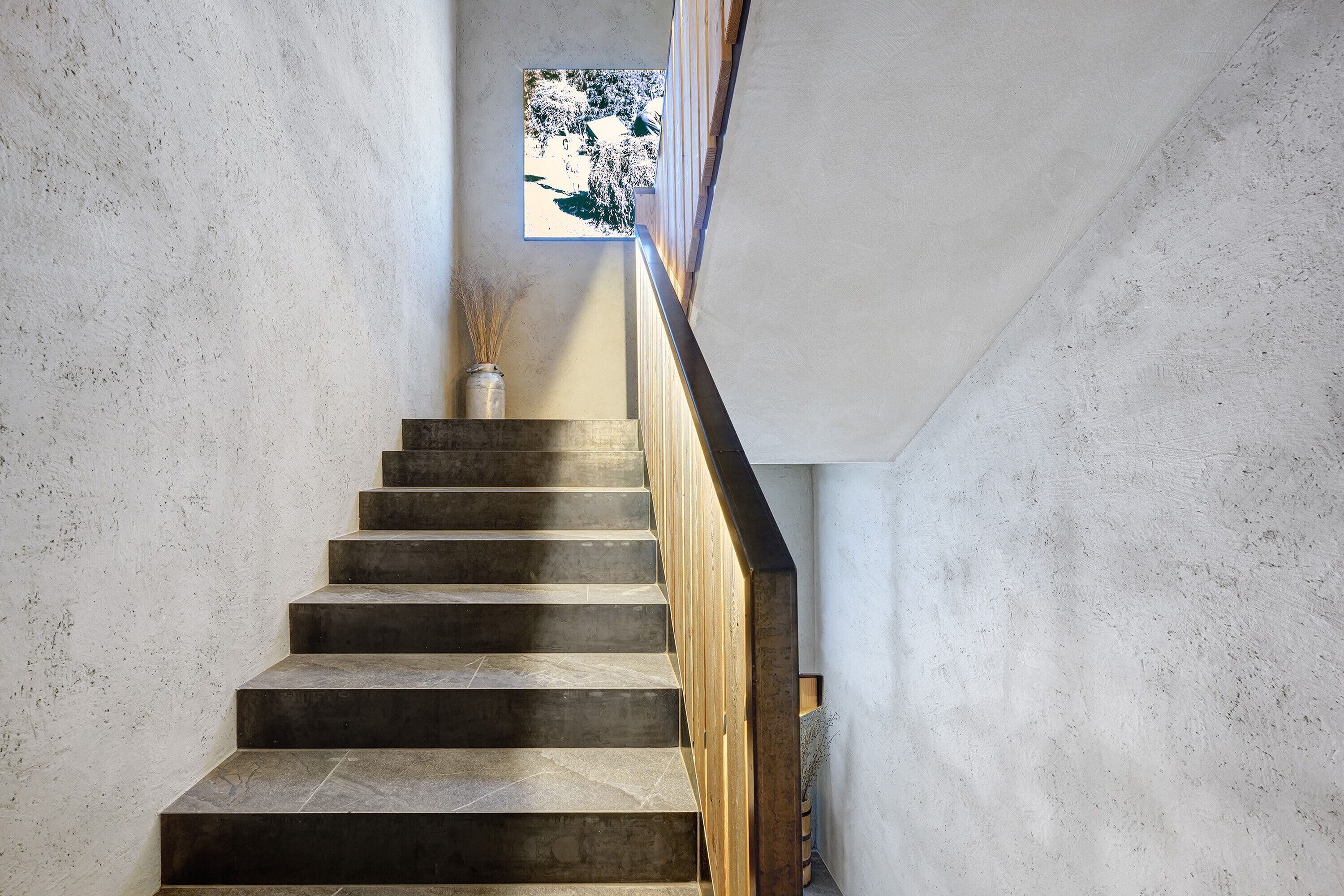A staircase with a wooden handrail and a vase of dried plants at the top.