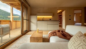 A modern interior with a wooden deck, a kitchen with a built-in sink, and a cozy seating area with a blanket. - Oberwidner Aura – Luxury Suite in Sarntal (Sarntal)