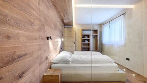 A modern bedroom with a wooden wall, a bed with white bedding, and a built-in wardrobe. - Oberwidner Aura – Luxury Suite in Sarntal (Sarntal)