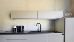 Una cocina con un lavamanos, una cafetera y una tetera sobre la encimera.