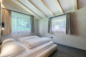 Un dormitorio con cama, dos ventanas con cortinas, techo de madera y pared texturizada.