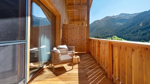 Un balcon en bois offrant une vue sur les montagnes, une porte vitrée et un canapé en osier agrémenté de coussins.