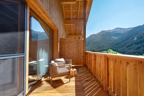A wooden balcony with a view of mountains, a glass door, and a wicker sofa with cushions. - Oberwidner Pura – Luxury Suite in Sarntal (Sarntal)