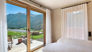 Ein Schlafzimmer mit einer großen Schiebetür, die auf eine Terrasse mit Sitzgelegenheit und Bergblick führt.