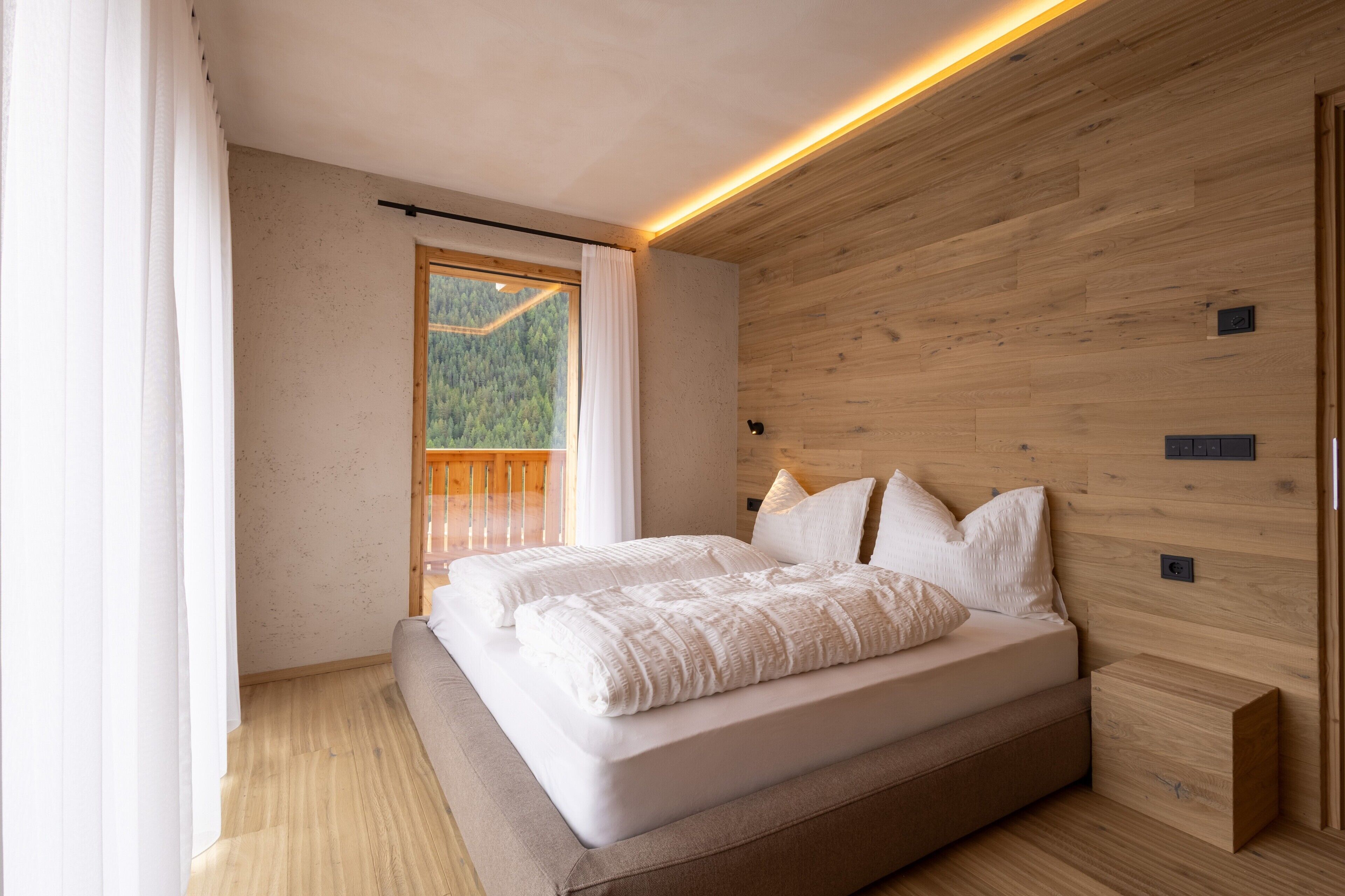 A bedroom with a large bed, wooden walls, and a window with a view of a forest.