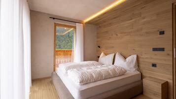A bedroom with a large bed, wooden walls, and a window with a view of a forest.