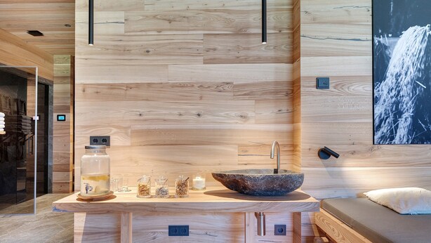 Ein modernes Badezimmer mit Holzwand, einem Waschbecken mit Natursteinbecken und einem Glasgefäß mit Wasserhahn.