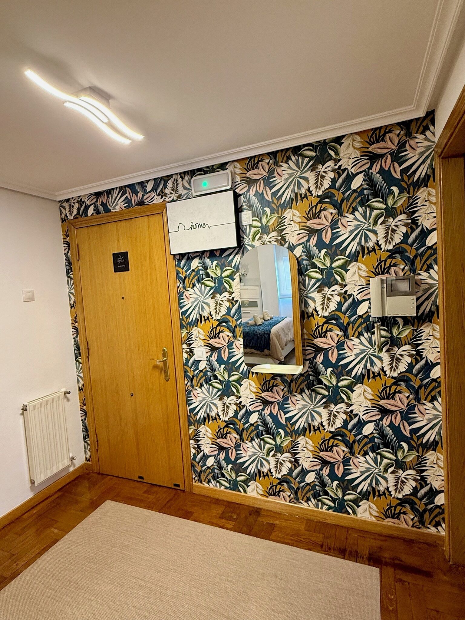 Une pièce avec une porte en bois, un radiateur, un miroir et un papier peint à motifs floraux.