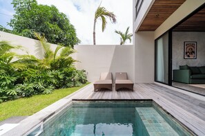 Un espace piscine extérieur moderne, doté de deux chaises longues, d’une terrasse en bois et d’une végétation luxuriante.