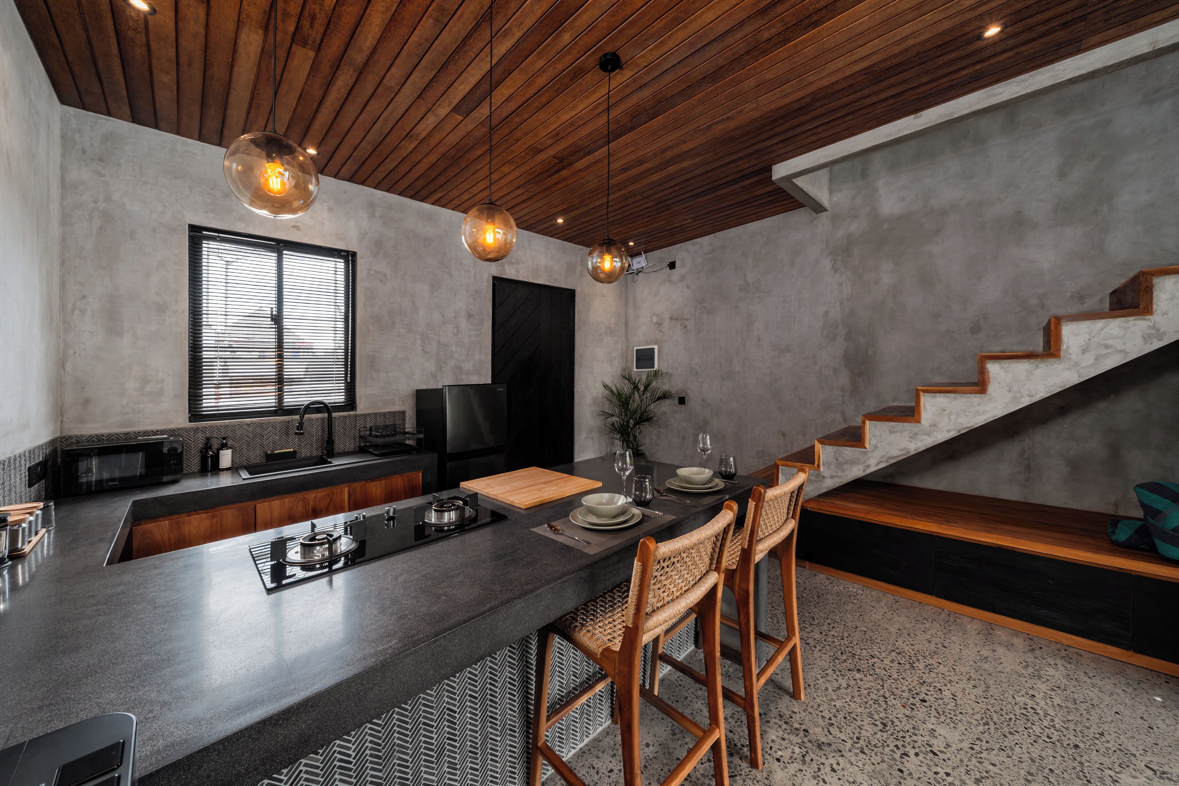 A modern kitchen with a central island, wooden ceiling, and a staircase leading to a loft area.