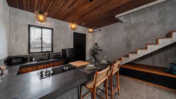 A modern kitchen with a central island, wooden ceiling, and a staircase leading to a loft area.