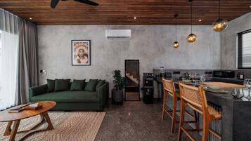 A modern living space with a green sofa, a wooden coffee table, a kitchen area with bar stools, and a ceiling fan.