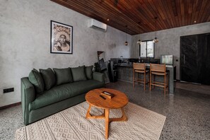 A modern living room with a green sofa, a wooden coffee table, and a kitchen area with a bar and seating. - Unique and Stylish Villa w/ Plunge Pool Near beach (Canggu)