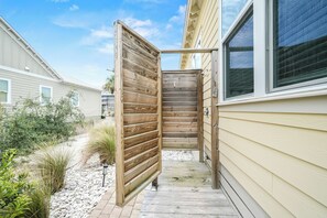 A wooden gate leading to a pathway, a house with beige siding, and a window with blinds. - New Coastal Retreat | Boardwalk, Fire Pit & Games (Port St. Joe)