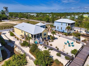 A beachfront property with two main buildings, a sandy beach area with lounge chairs, and a wooden boardwalk. - New Coastal Retreat | Boardwalk, Fire Pit & Games (Port St. Joe)