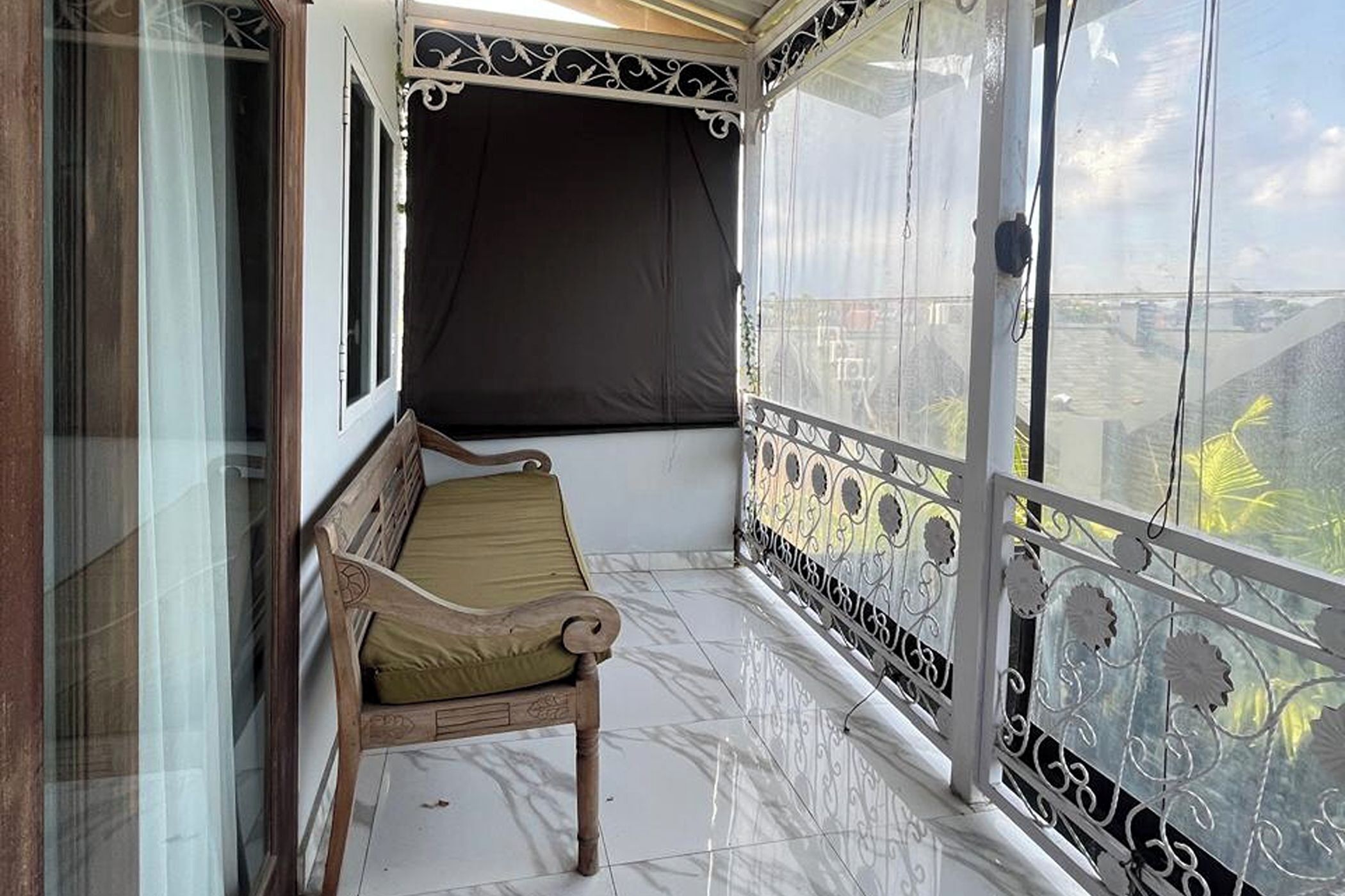 A balcony with a wooden bench, a black curtain, and a glass railing with decorative patterns.