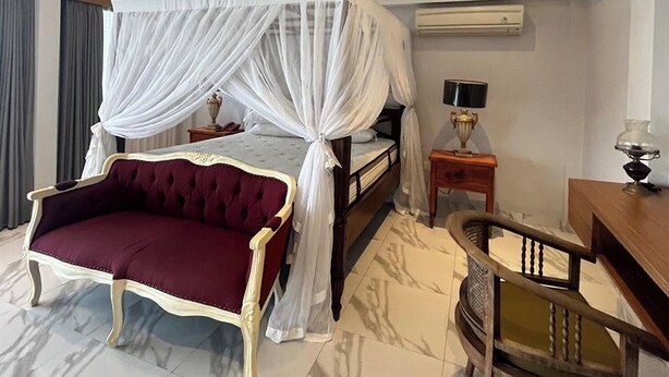Ein Hotelzimmer mit Himmelbett, Chaiselongue, Schreibtisch und Sessel.