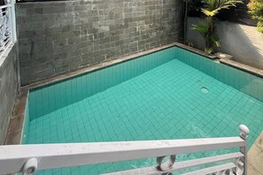 En lille, rektangulær swimmingpool med flisebelagt bund, omgivet af en stenvæg og et hvidt gelænder.