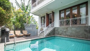 A swimming pool with a wooden deck, lounge chairs, and a staircase leading to a balcony.