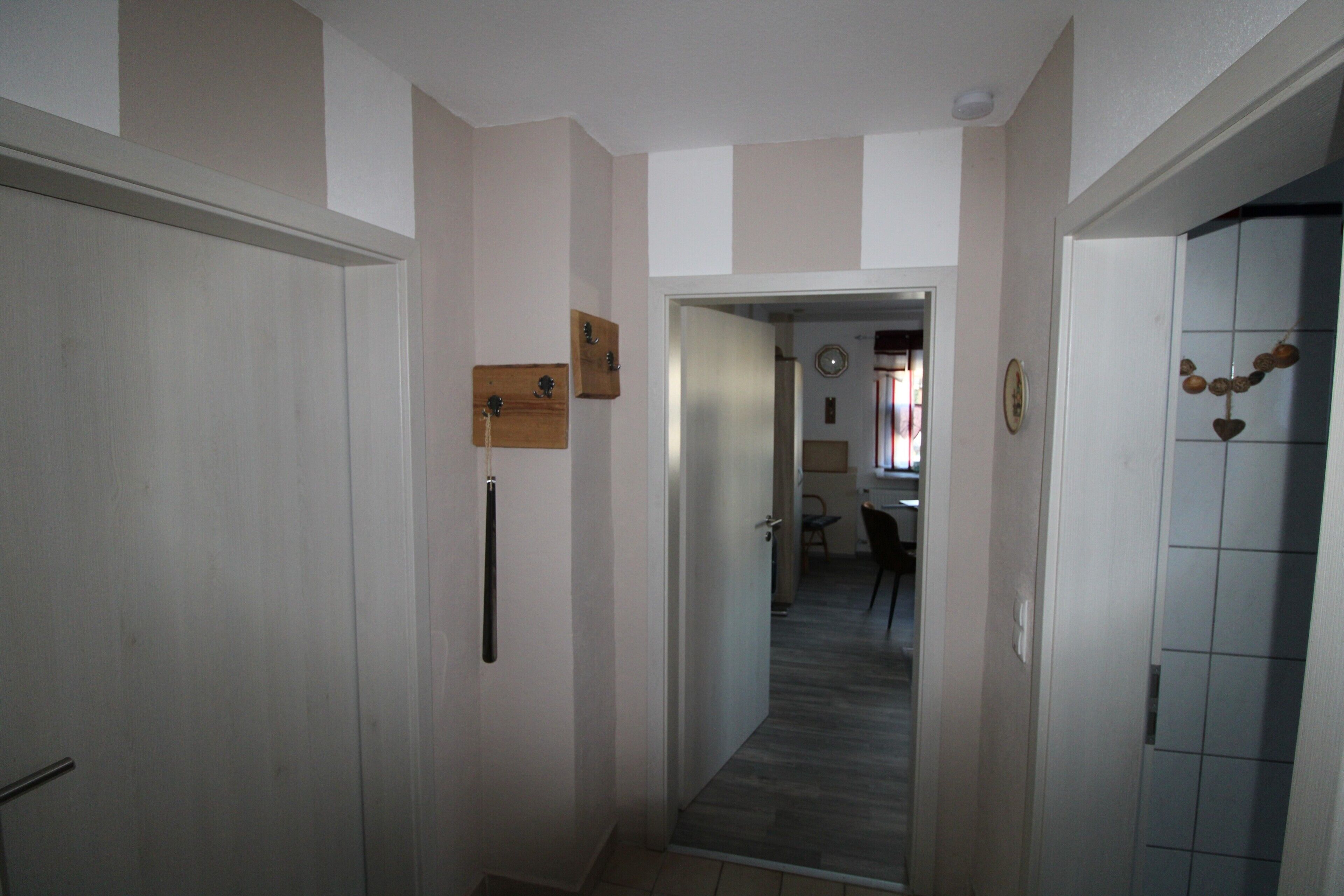 A hallway with a door on the left, a wooden shelf, and a tiled wall on the right.
