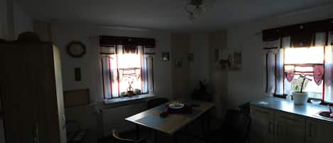 Uma sala de jantar com mesa, cadeiras, um relógio e janelas com cortinas.