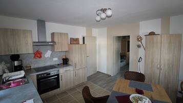 Une cuisine compacte dotée d’appareils électroménagers modernes, un coin repas avec une table dressée pour deux personnes, et un couloir menant à une autre pièce.