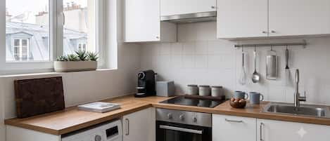 Une cuisine moderne équipée d’un lave-linge, d’un four et d’une fenêtre donnant sur des immeubles.