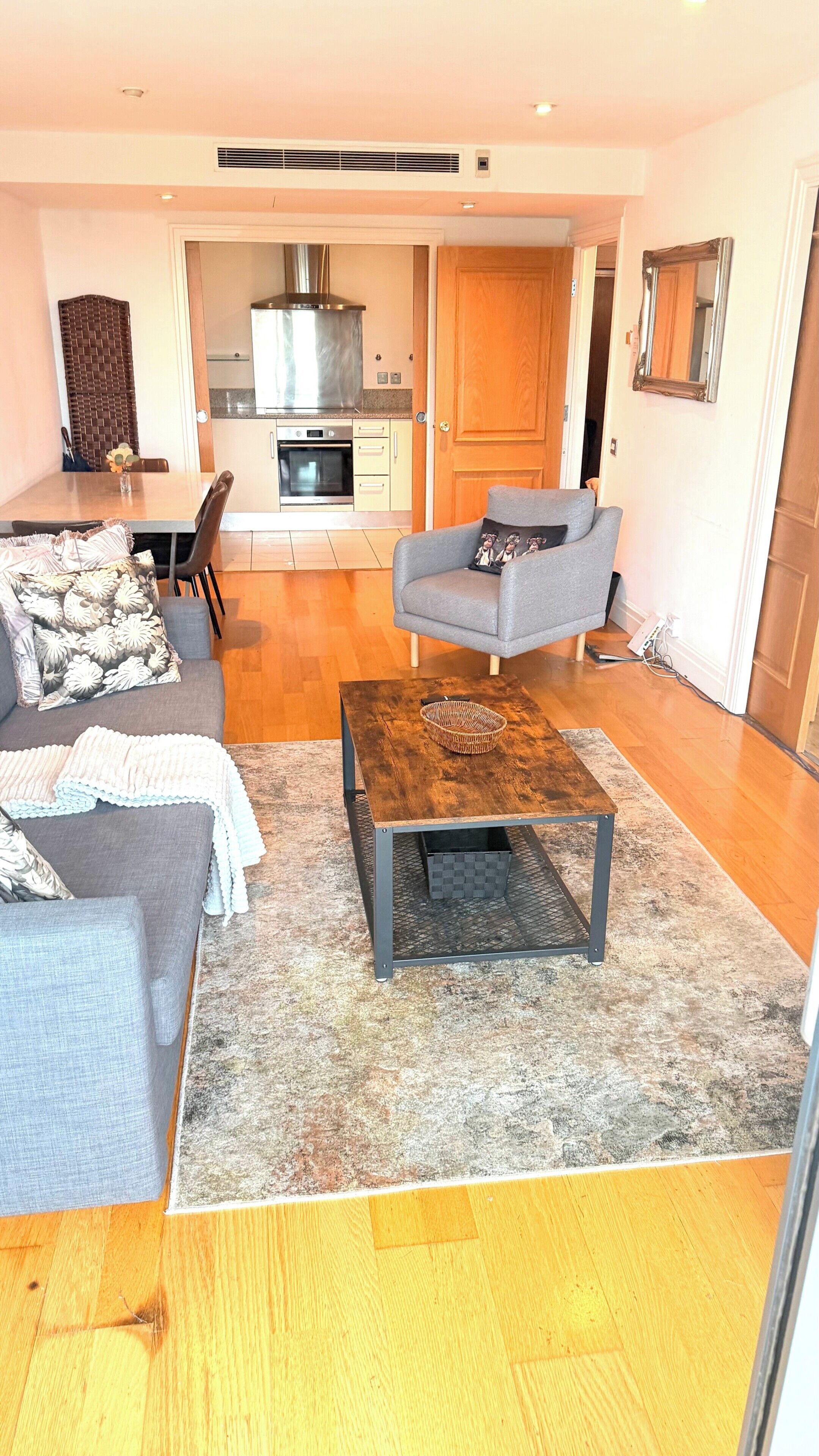 Una sala de estar con sofá, sillón, mesa de centro y una cocina al fondo.