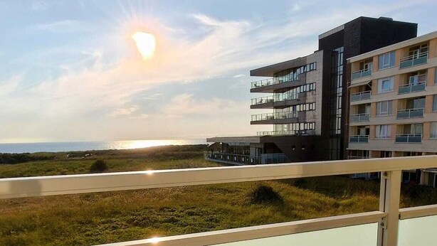 A balcony with a view of a beach and a building. - The beach, the ocean, and the dunes right outside your door! This Duinparel apartment is located on the 2nd floor of the Kennedyflat complex. This apartment is on the ground floor and features one bedroom, a kitchen, a bathroom, and a west-facing balcony. (Egmond aan Zee)