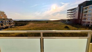 A balcony with a view of a grassy area, a body of water, and modern buildings. - The beach, the ocean, and the dunes right outside your door! This Duinparel apartment is located on the 2nd floor of the Kennedyflat complex. This apartment is on the ground floor and features one bedroom, a kitchen, a bathroom, and a west-facing balcony. (Egmond aan Zee)