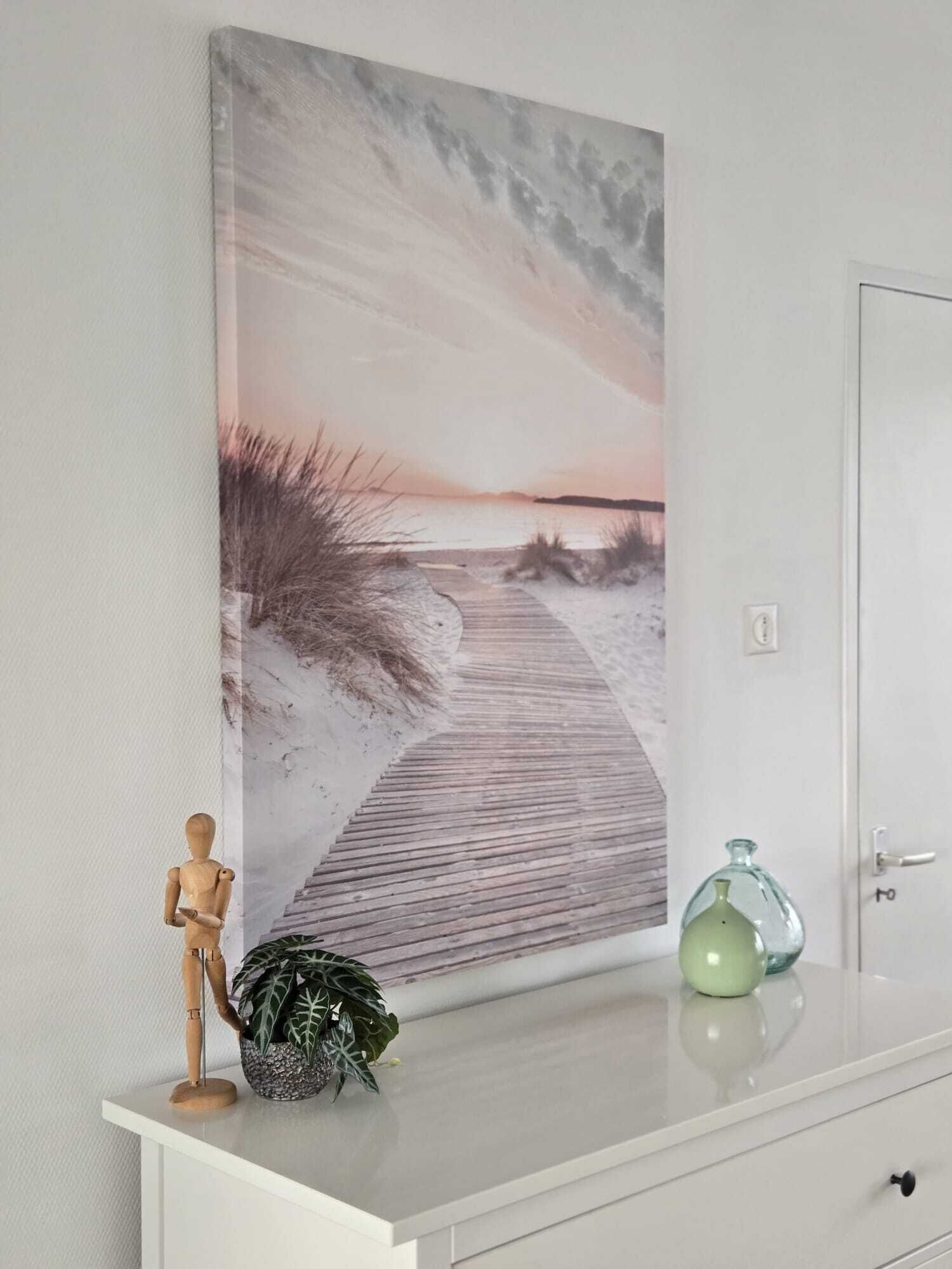 Une commode blanche ornée d’un tableau représentant une scène de plage, un mannequin en bois et une bouteille en verre.