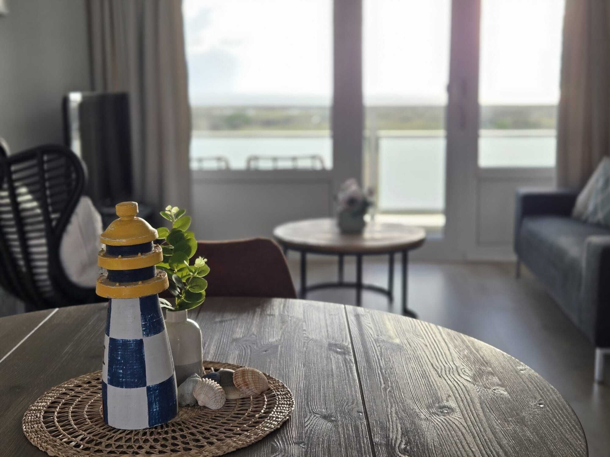 Une table en bois ornée d’un phare décoratif, d’un vase et de quelques coquillages.