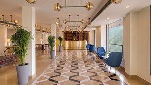 Un vestíbulo de hotel con piso de diseño geométrico, sillas azules, un mostrador de recepción y plantas en macetas.