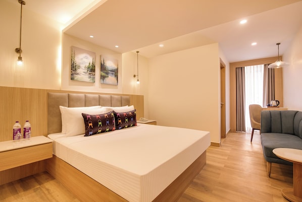A hotel room with a large bed, bedside tables, a desk, a chair, and a dining area.