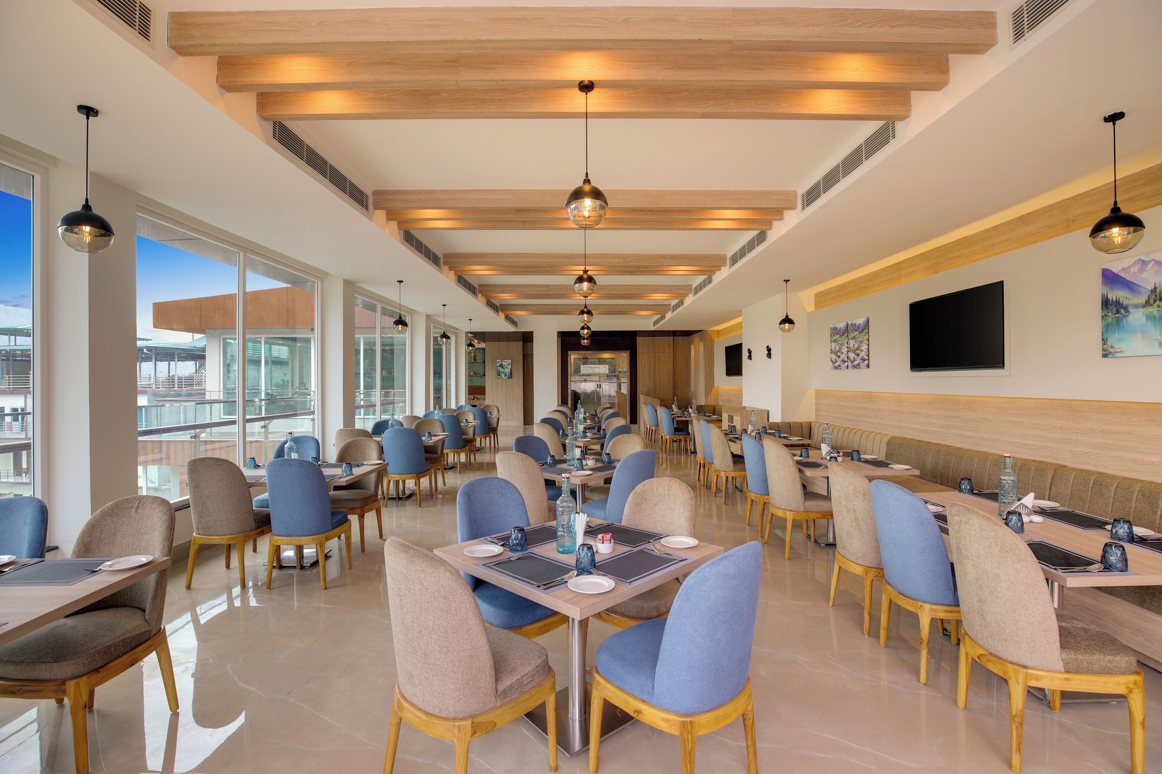 Un comedor amplio con varias mesas y sillas, ventanas grandes que ofrecen vistas y un techo alto con vigas de madera.