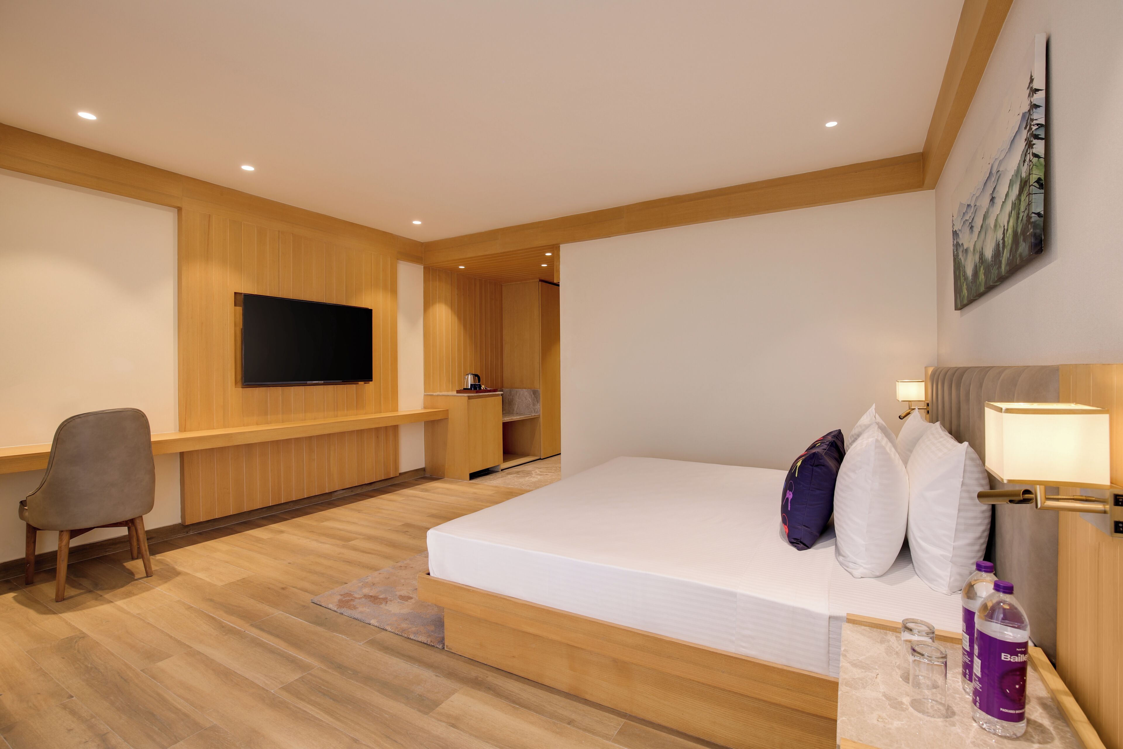 A hotel room with a bed, a desk, a chair, a television, and a painting on the wall.