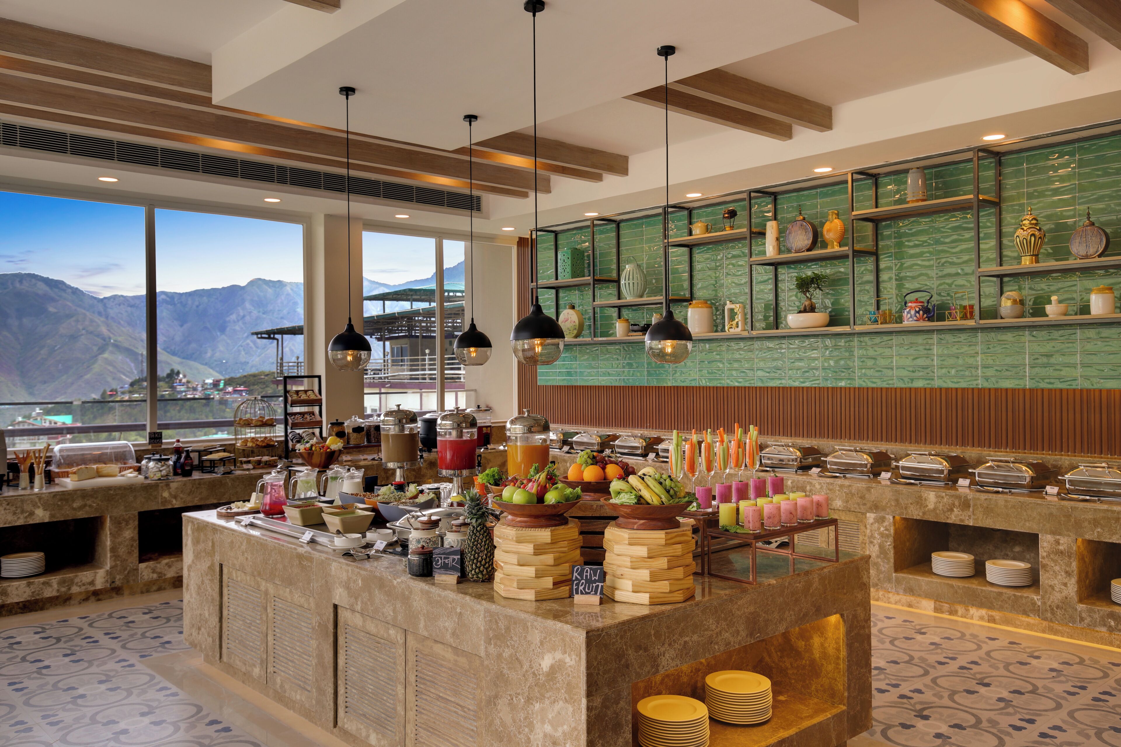A buffet area with a view of mountains, a variety of food items, and a green tiled backsplash.