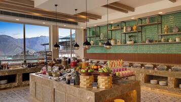 A buffet area with a view of mountains, a variety of food items, and a green tiled backsplash.