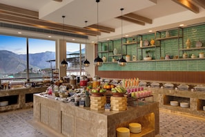 A buffet area with a view of mountains, a variety of food items, and a green tiled backsplash.