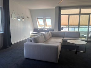 A modern living room with a sectional sofa, a round coffee table, and a large window offering a view.