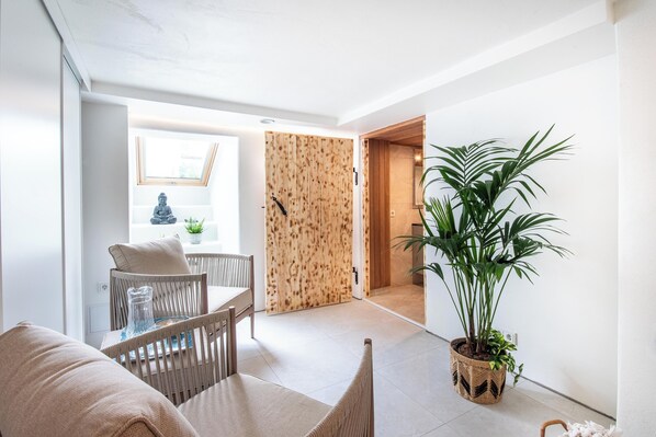 A modern living room with a dining area, a large potted plant, and a wooden door leading to another room.