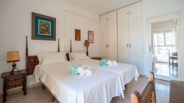 A hotel room with two beds, a nightstand, a lamp, and a view of the outside. - Perla 5 - Charming Front-Row Apartment (Fuengirola)